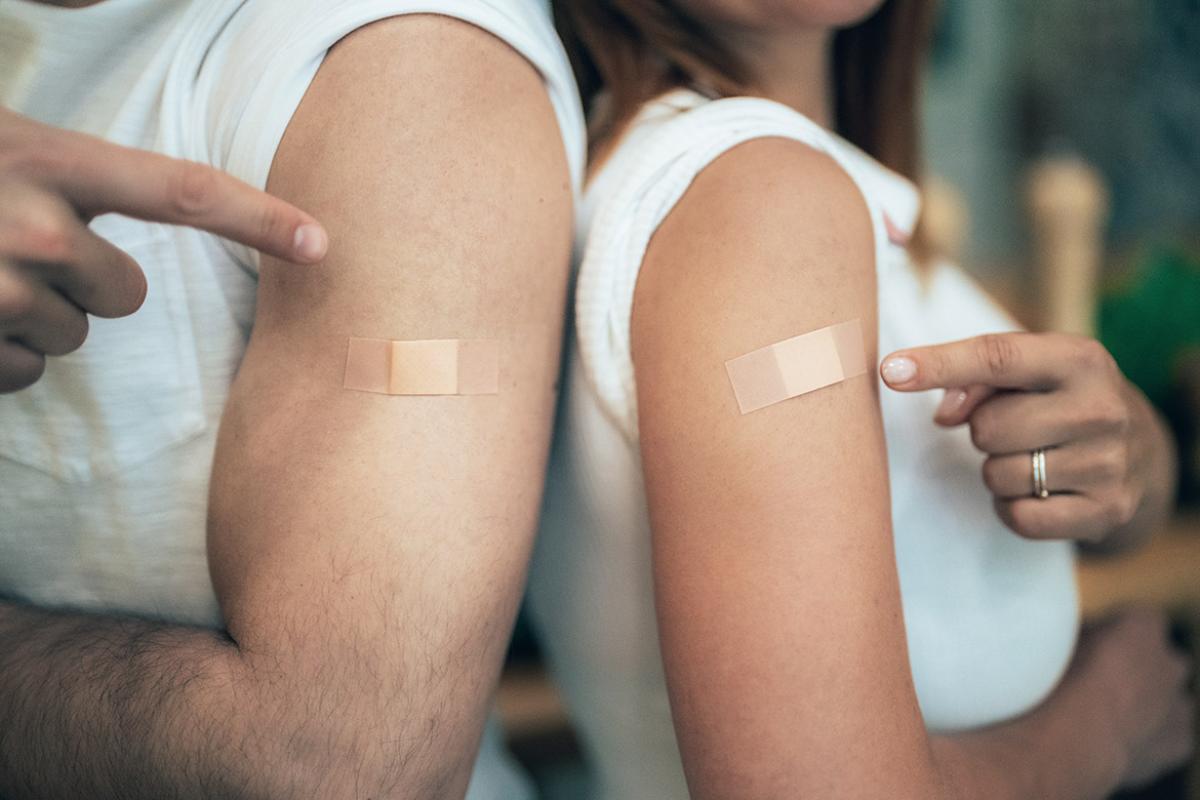 Two people pointing at their arms where they received a vaccine
