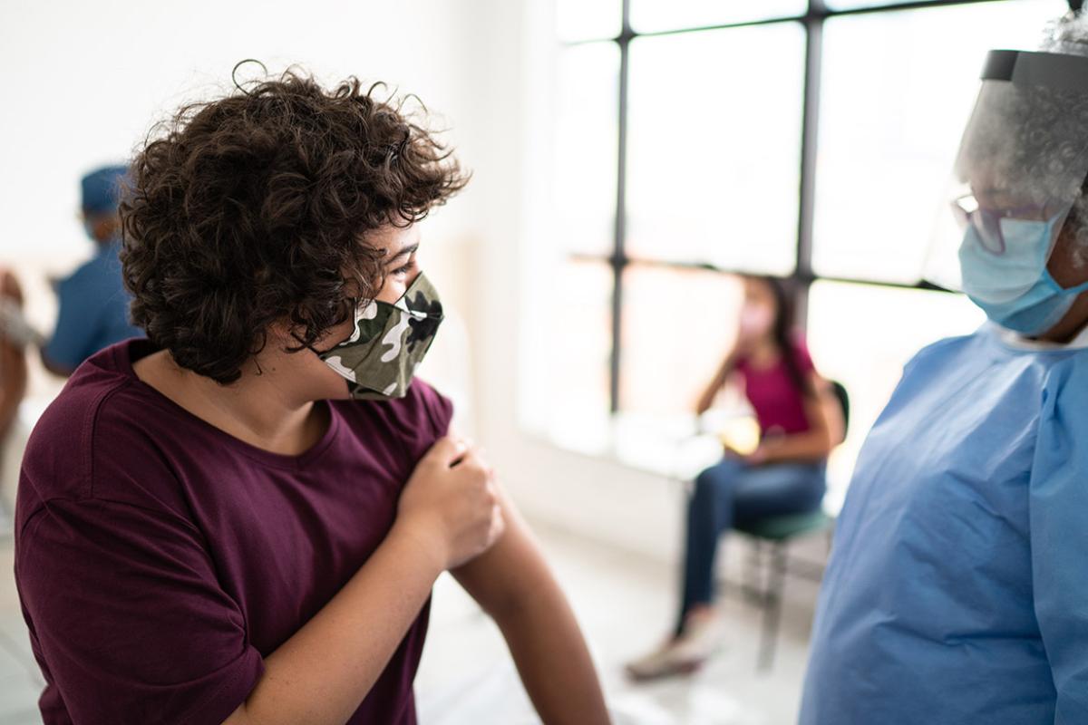 Teen with a face mask talking to health professional after receiving a vaccine