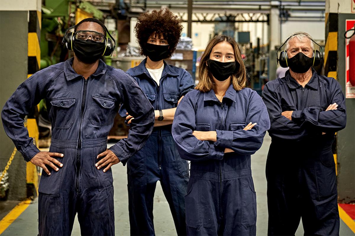 Group of metal workers in coveralls, protective eyewear, ear protectors, and face masks 