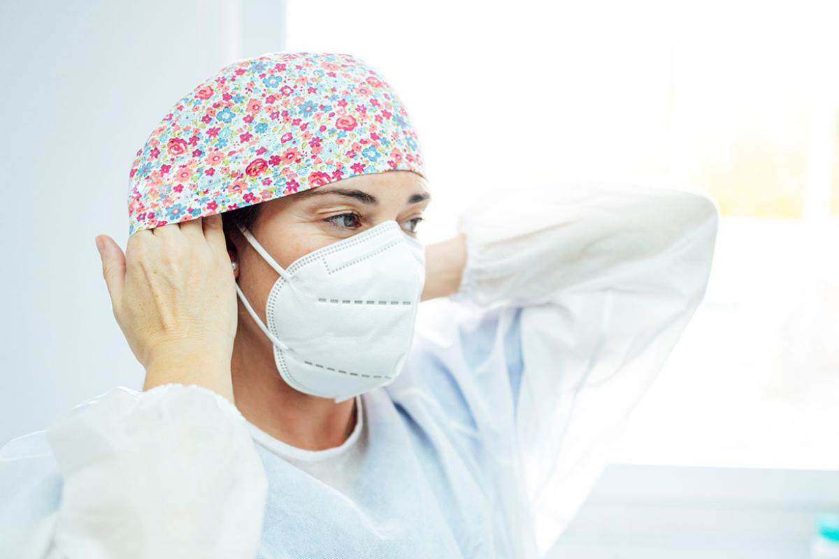 Health professional wearing face mask and adjusting surgical cap