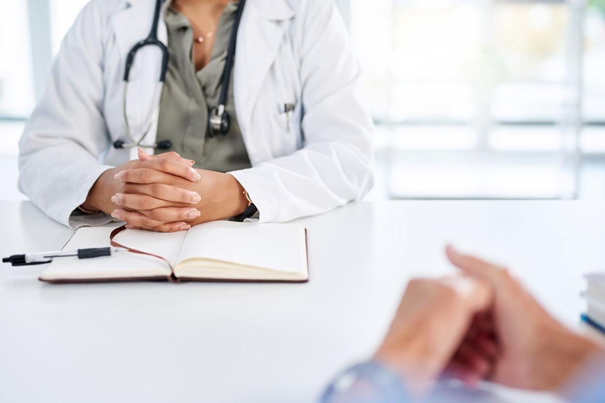 Physician with folded hands across the table from another individual