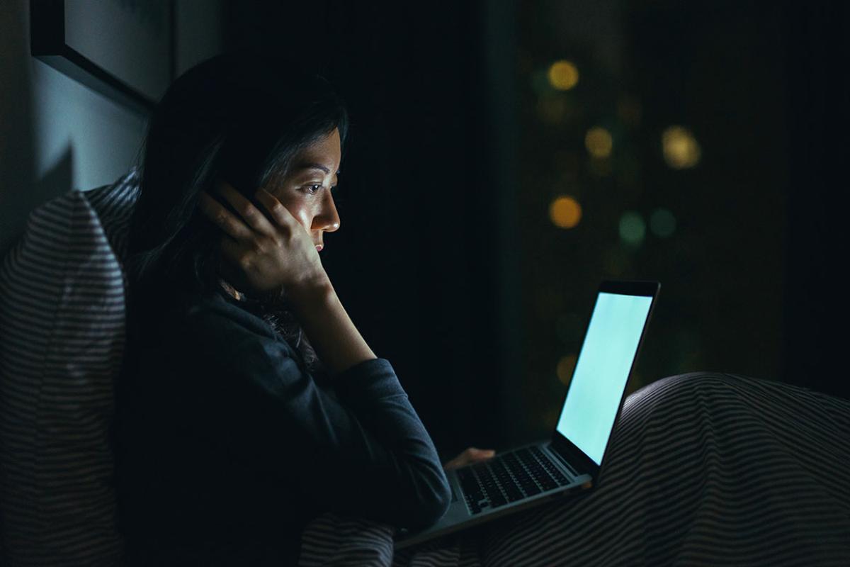Person sitting in a dark room, looking at a laptop