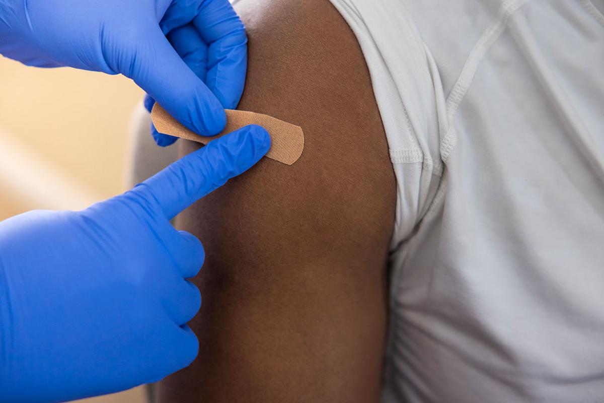 Health care professional applying adhesive bandage to person's upper arm