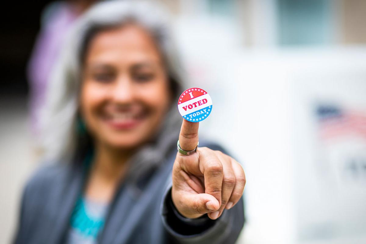 Smiling person with an "I Voted" sticker on their finger