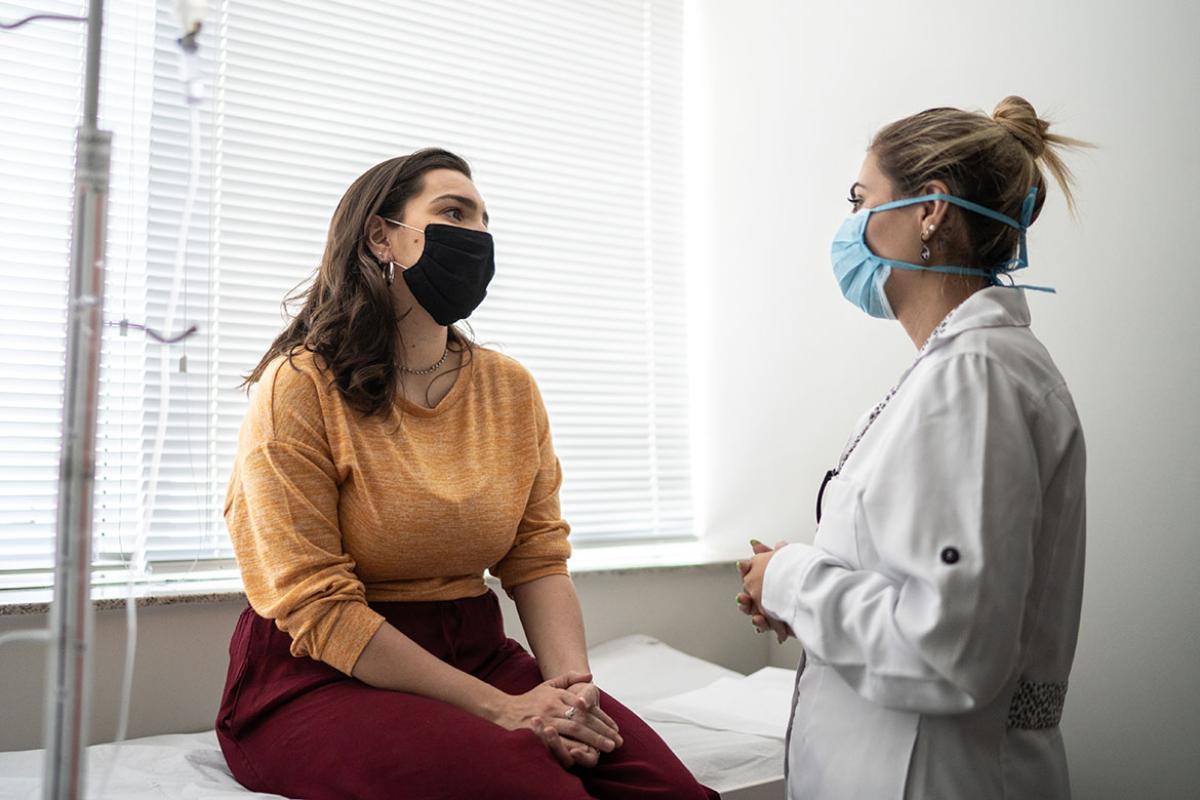Masked physician and patient speaking in examination room