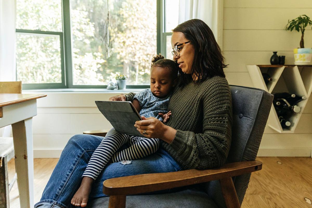 Person sitting with child on lap, both looking at a tablet device