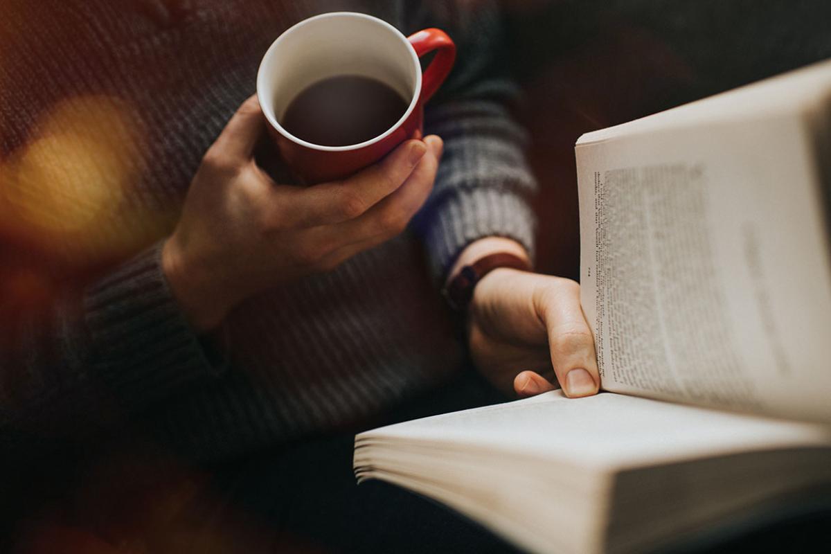 Person reading a book and drinking a hot drink from a mug