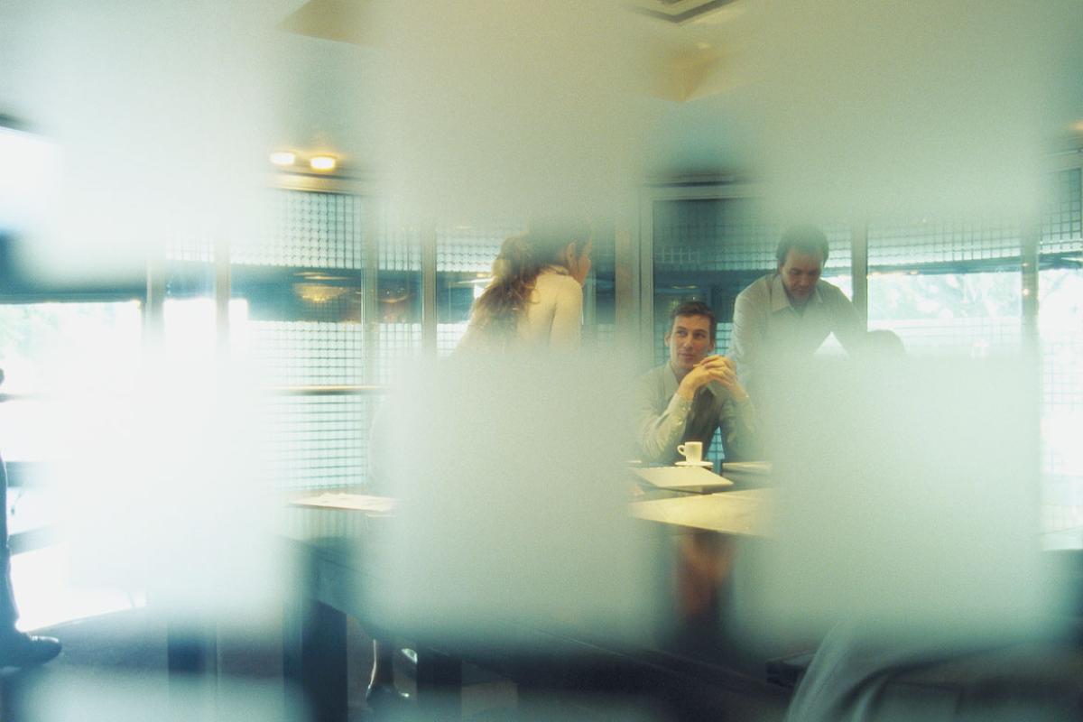 People in conference room, seen through semi-opaque glass wall 