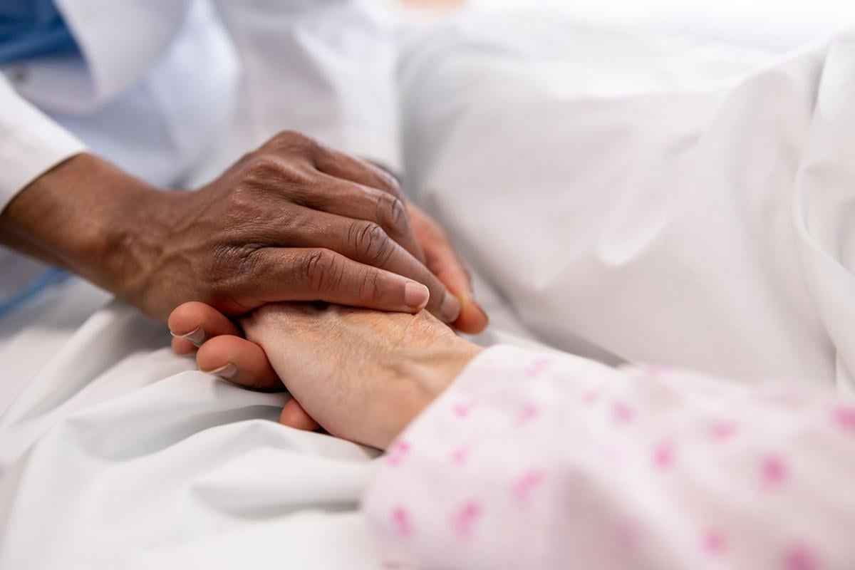 Health care worker holding the hand of a person in a hospital bed