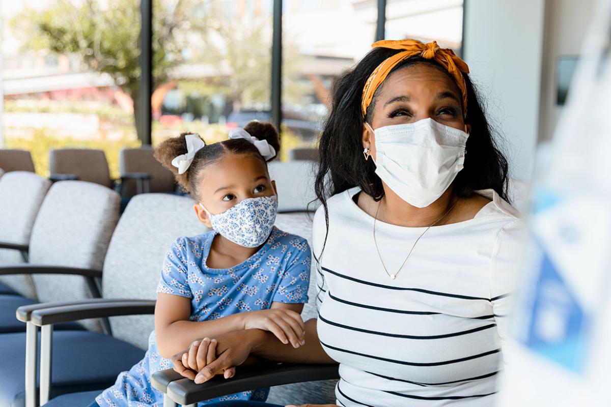 Woman and child patients, both wearing masks, waiting to be seen by doctor.