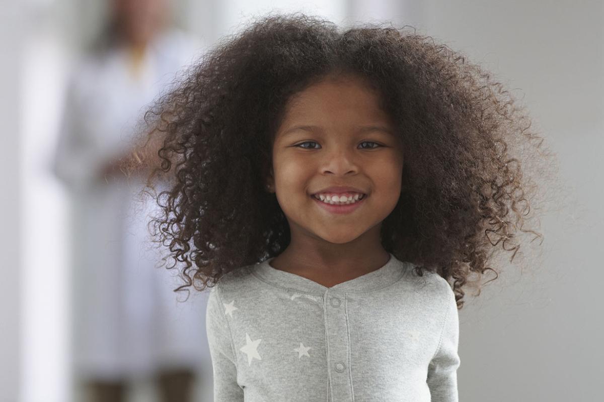 African-American girl smiles while a doctor stands behind her