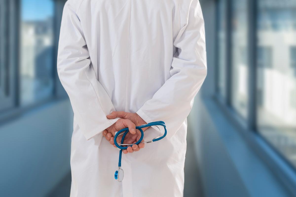 A male doctor holding a stethoscope in his hands behind his back