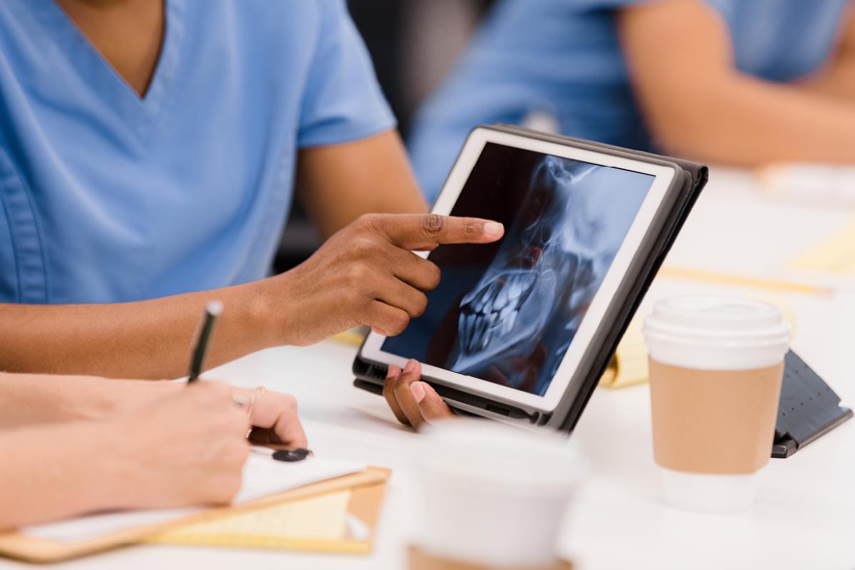 Black woman medical professional pointing to a tablet with an x-ray of a person’s teeth