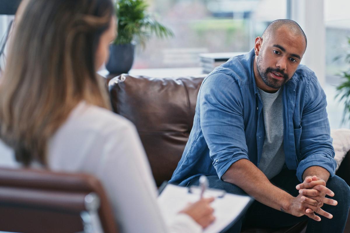 A man sitting on a couch talking to a female doctor who is taking notes