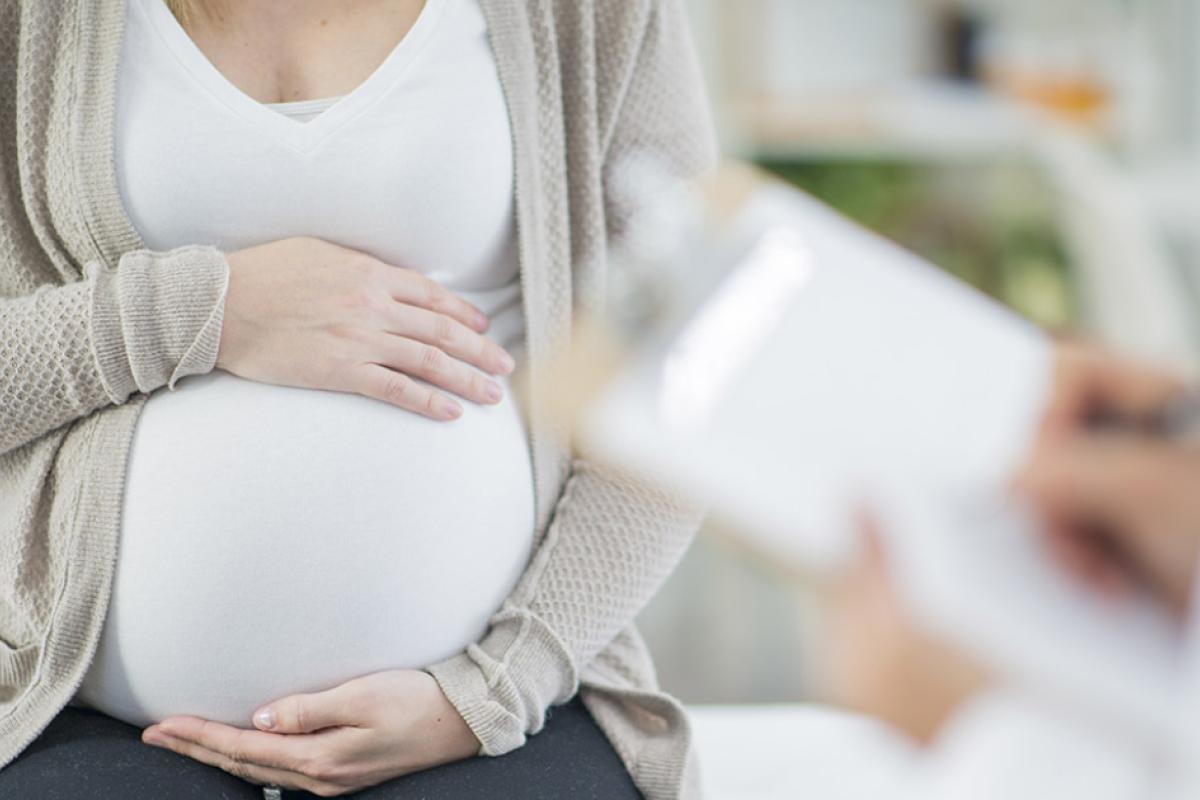 Pregnant woman holding her belly with two hands while consulting with a physician