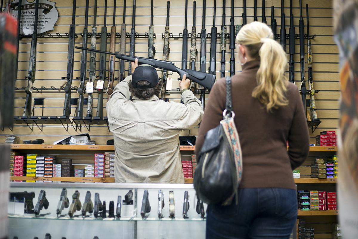 A sales person removes a rifle from the wall of a gun shop