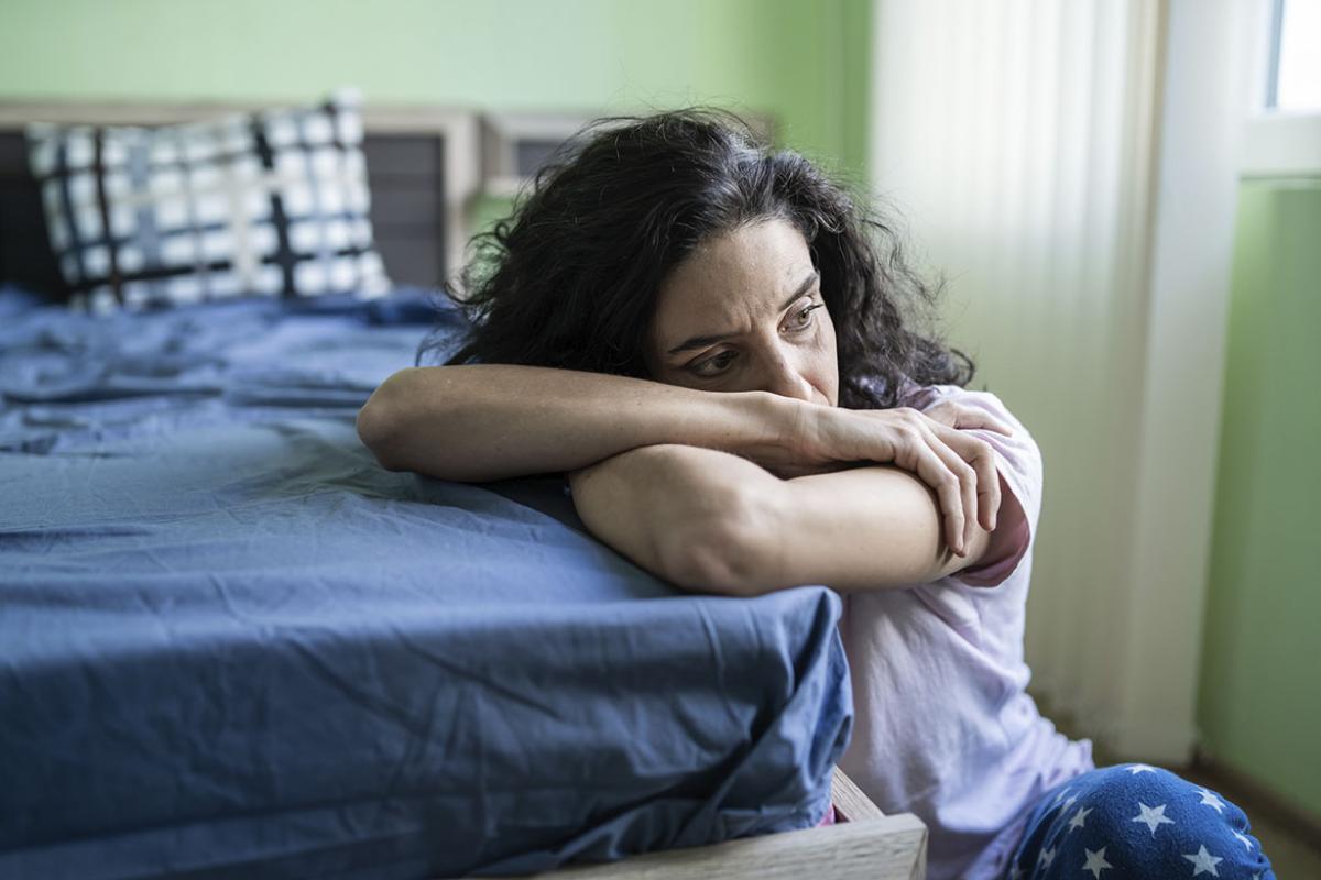 Despondent woman with arms crossed resting head on mattress