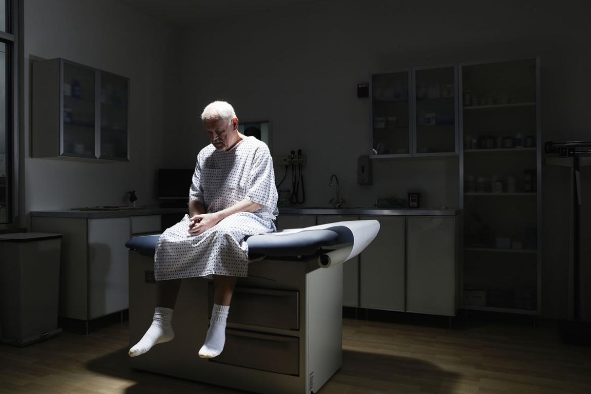 Senior patient sitting on examination table, looking down