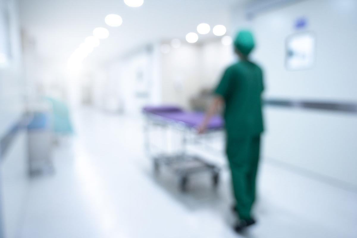 Figure pushing an empty hospital bed down a hallway