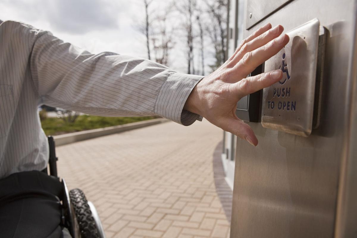 Businessperson in a wheelchair pushing a button to open a door 