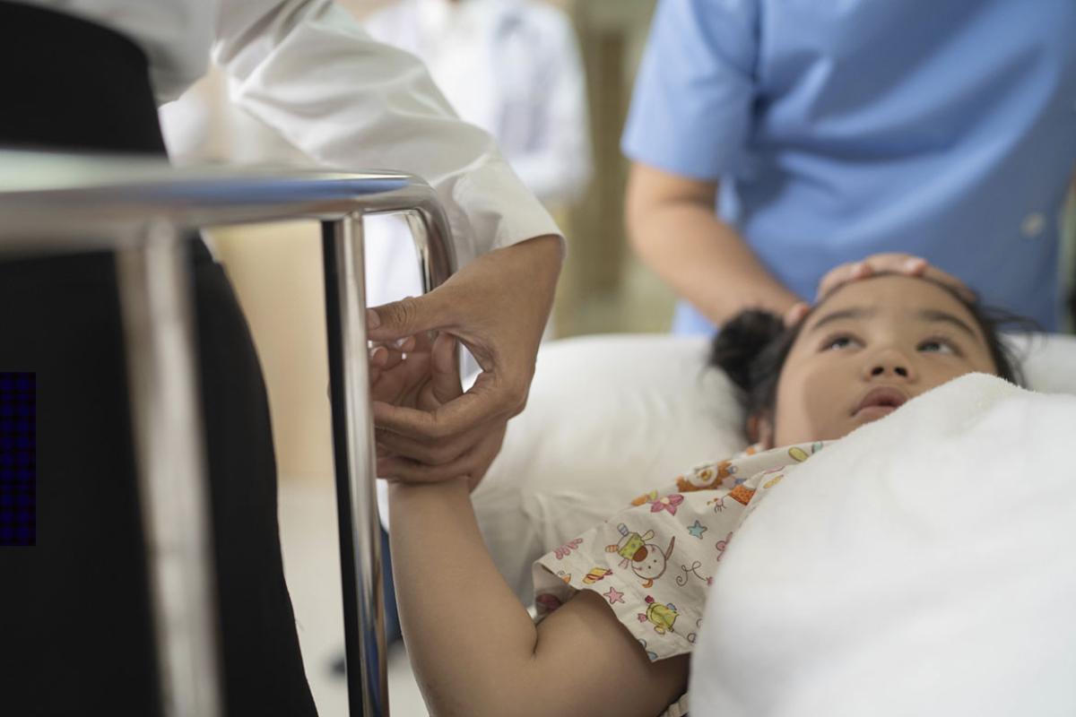 Child in a hospital bed holding a caregiver's hand