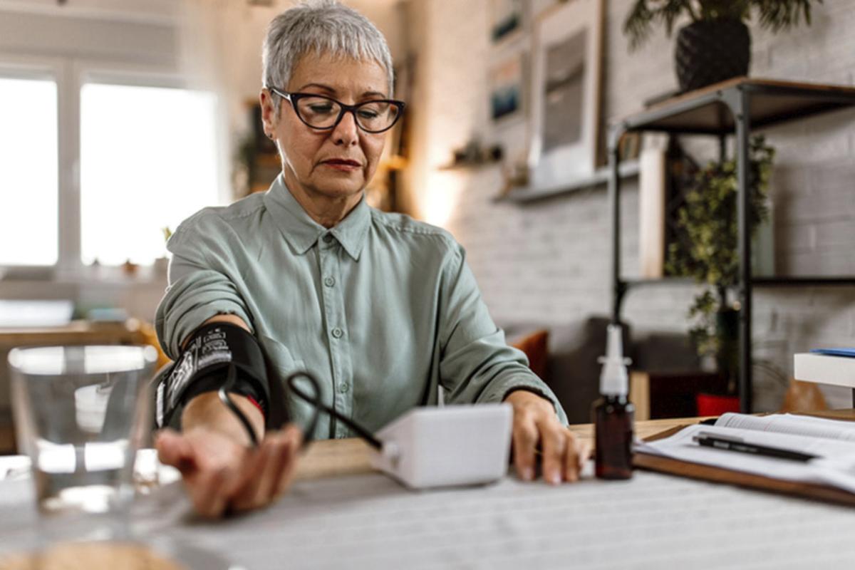 Senior woman sitting at a table and measuring blood pressure at home