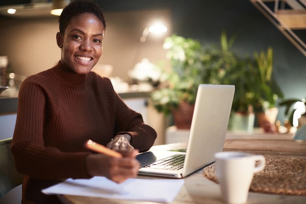 Smiling person holding a pen and working in front of a laptop