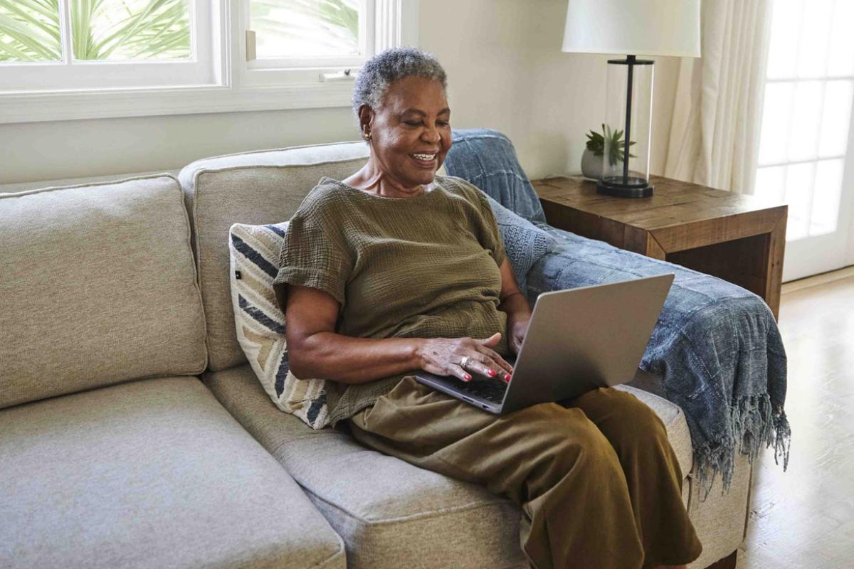Smiling woman sits on couch while typing on laptop