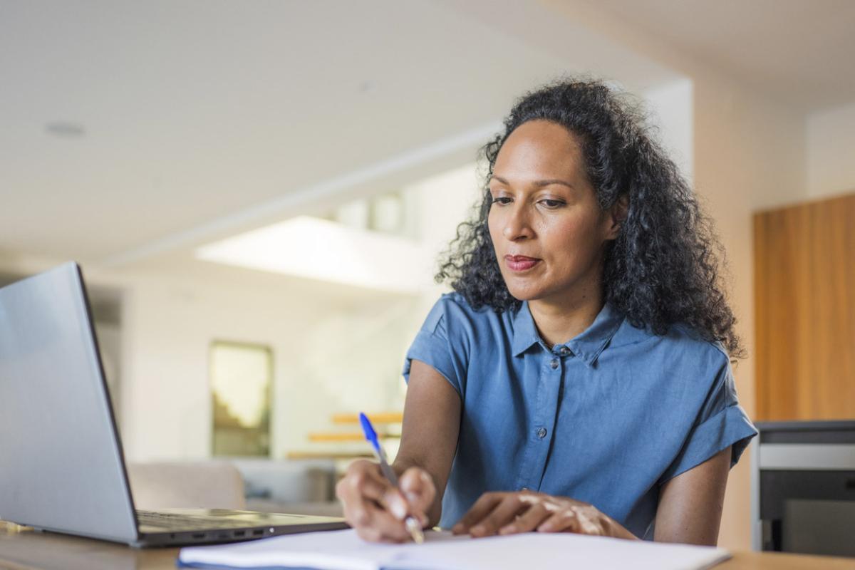 Woman writes while in front of laptop