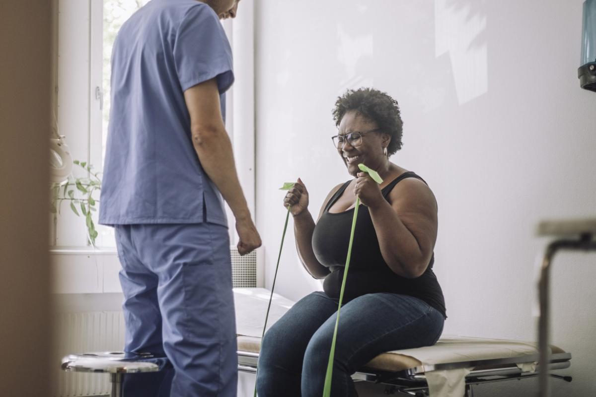 Physical therapist standing by patient exercising with resistance band