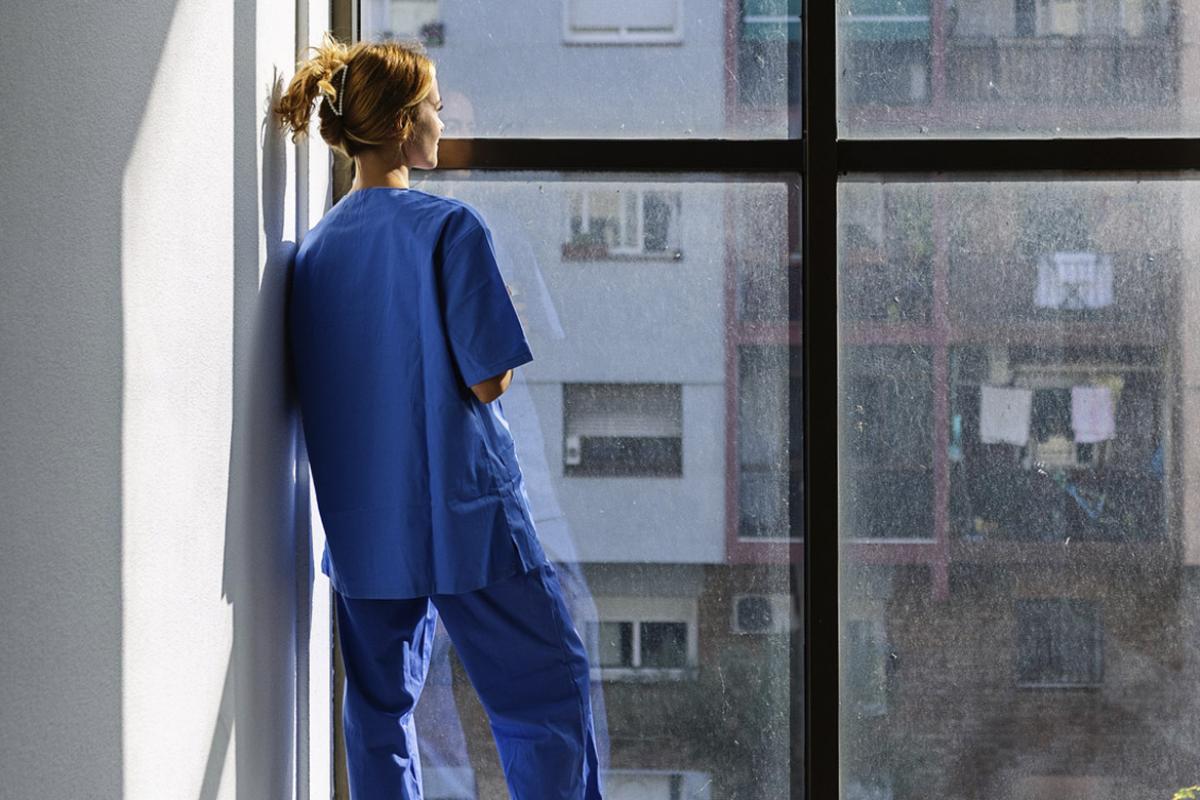 Healthcare worker in scrubs looking out the window