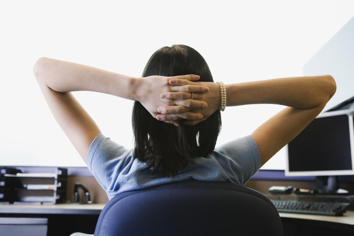 Person sits at a desk with hands clasped behind head