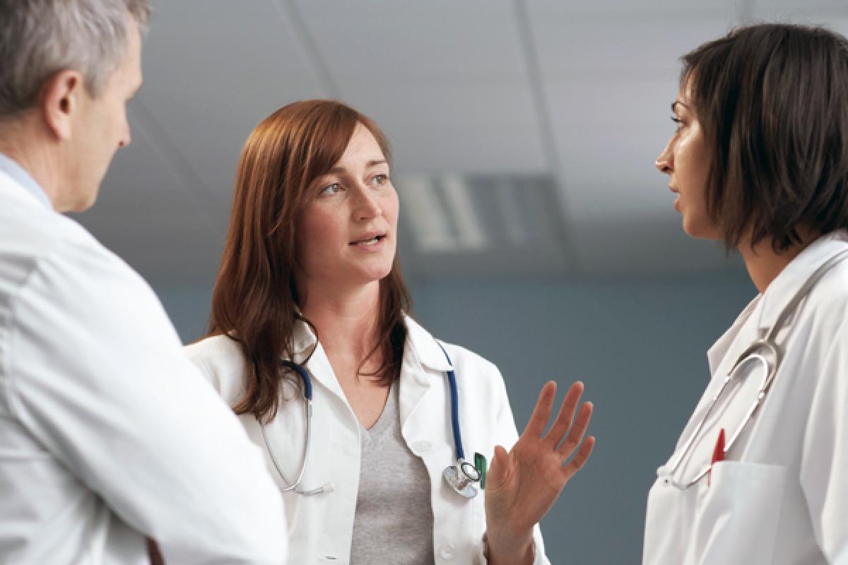 One male and two female physicians standing in a group while talking.