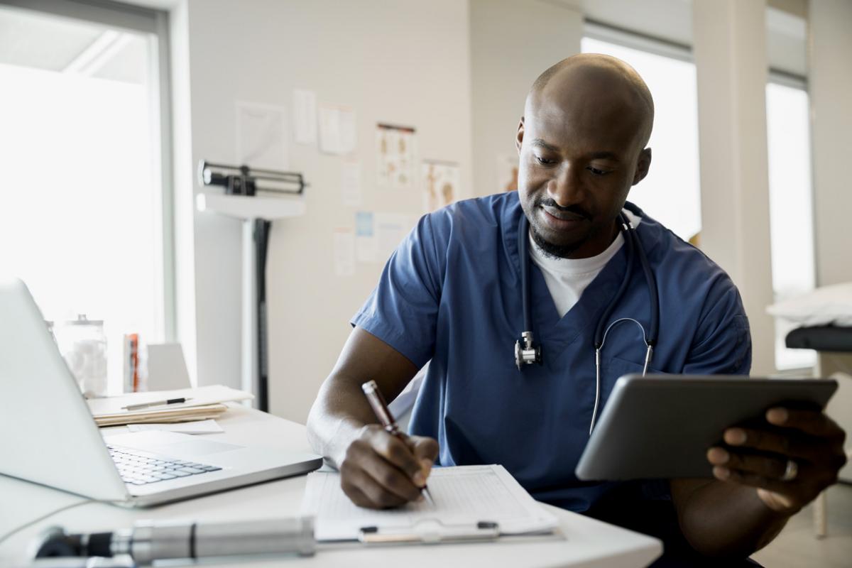 A male doctor in scrubs looks at PolicyFinder on his tablet.