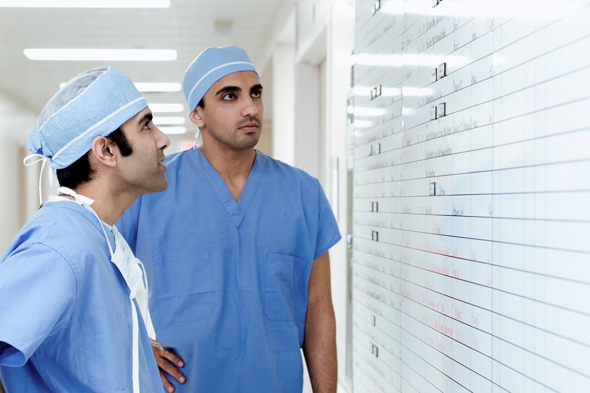 Two residents in surgical scrubs examine a whiteboard.