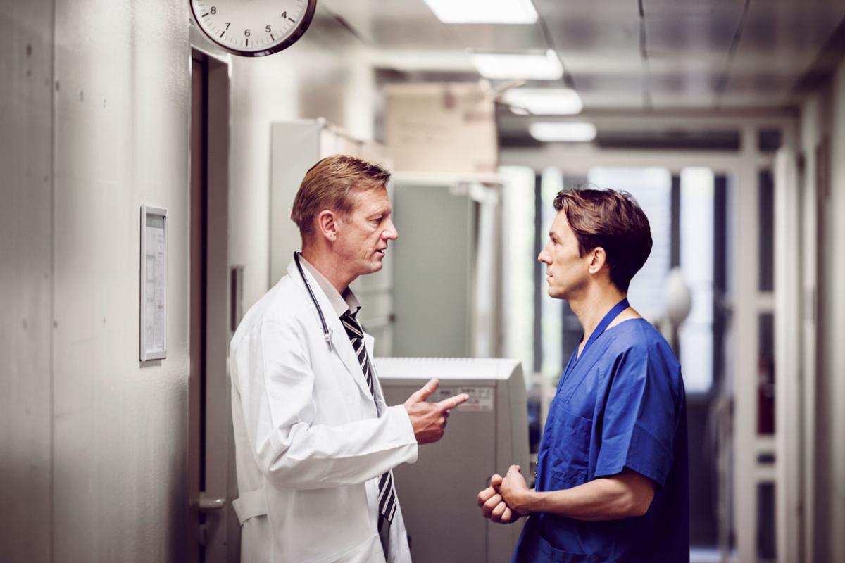 Physician speaking to resident in hospital hallway.