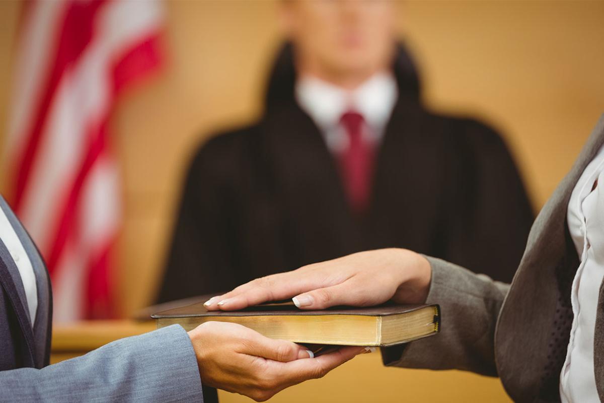 Hands being sworn in on a book in court.