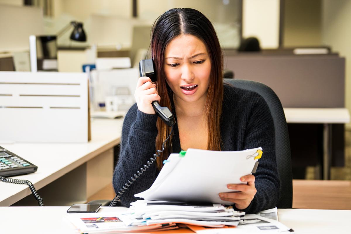 Woman on phone with a stack of papers in front of her.