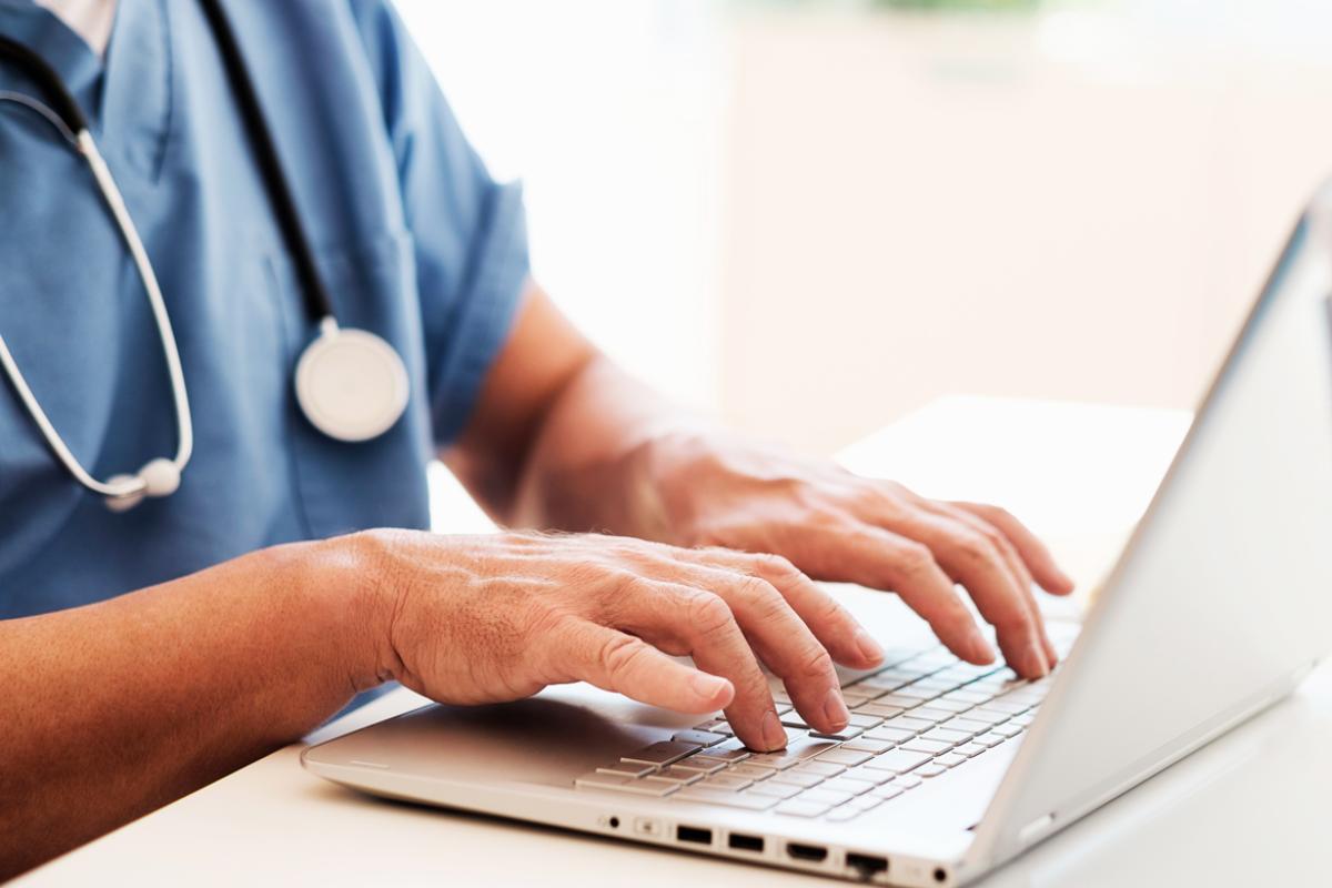 Physician entering data into a laptop.