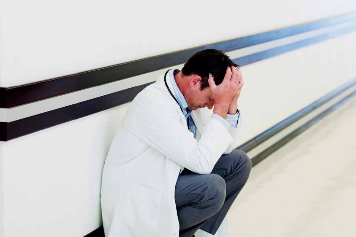 Dejected physician leans against a wall.