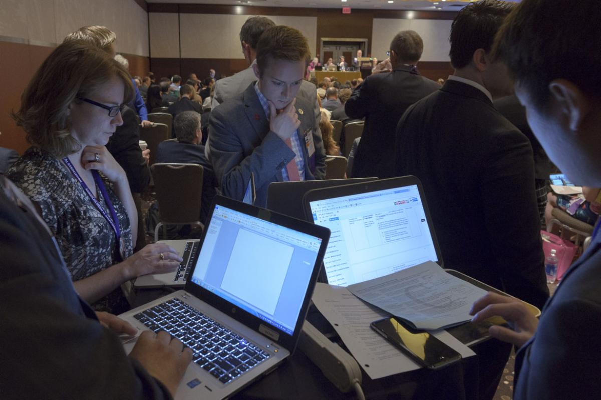 Physicians gathered around opened laptops working. 