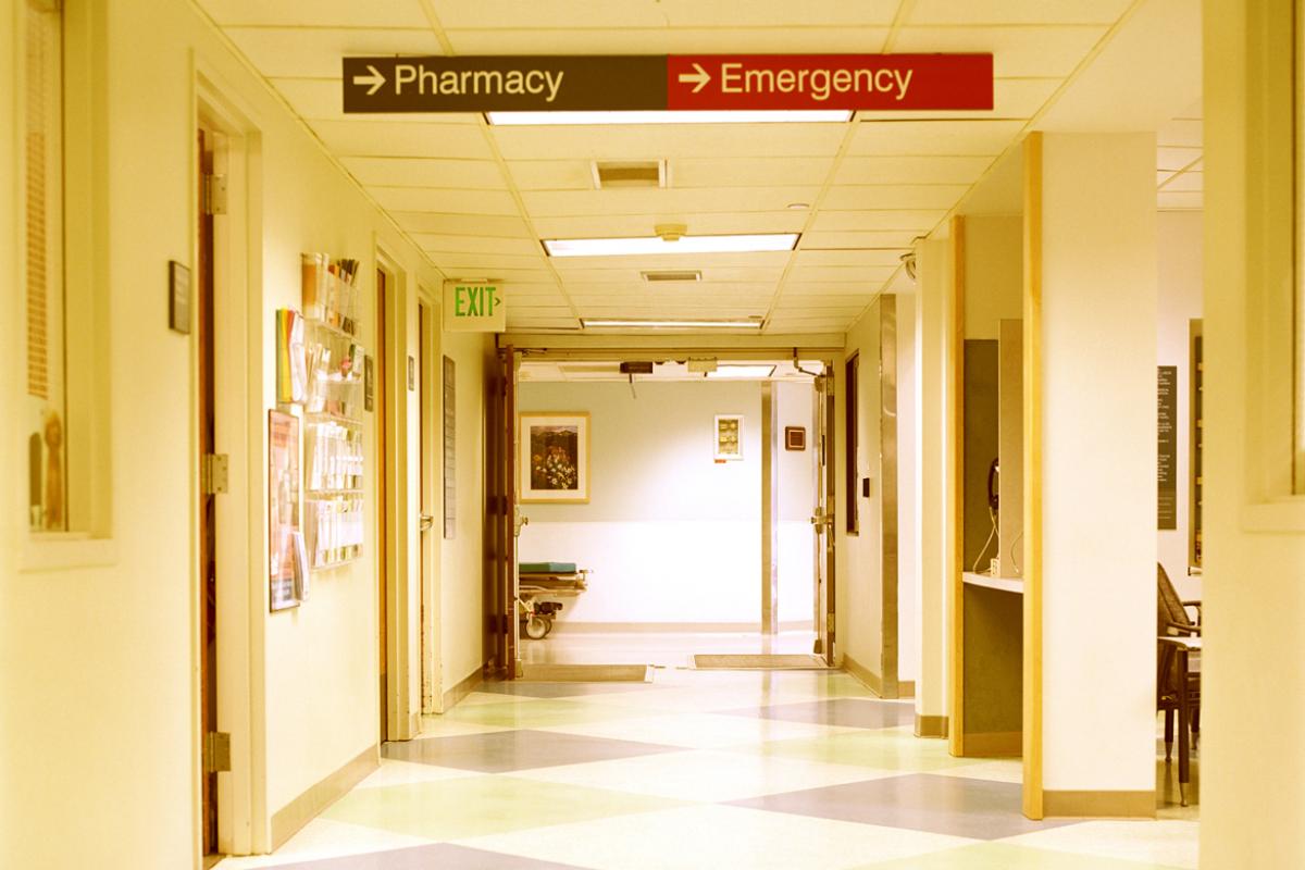 Interior hallway of a hospital with sign pointing to 'emergency' department. 