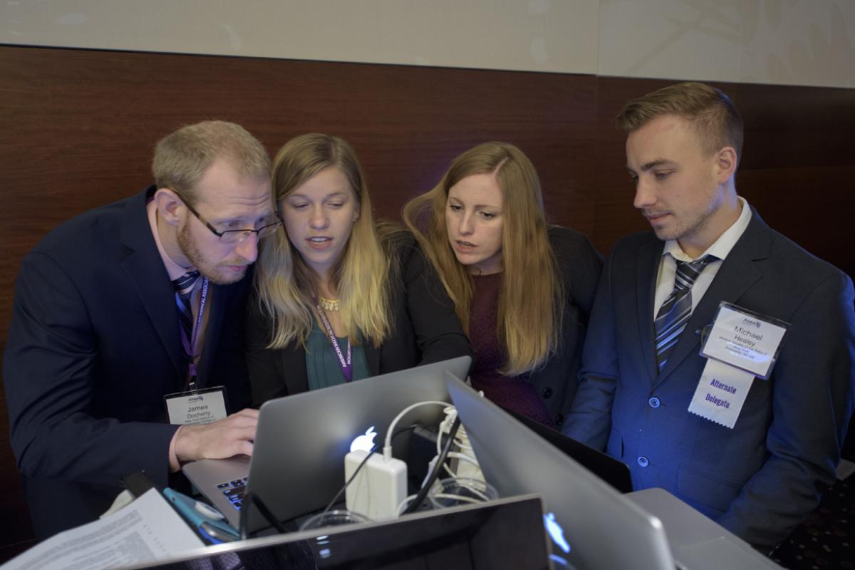 A group of AMA delegates review something in front of a laptop.