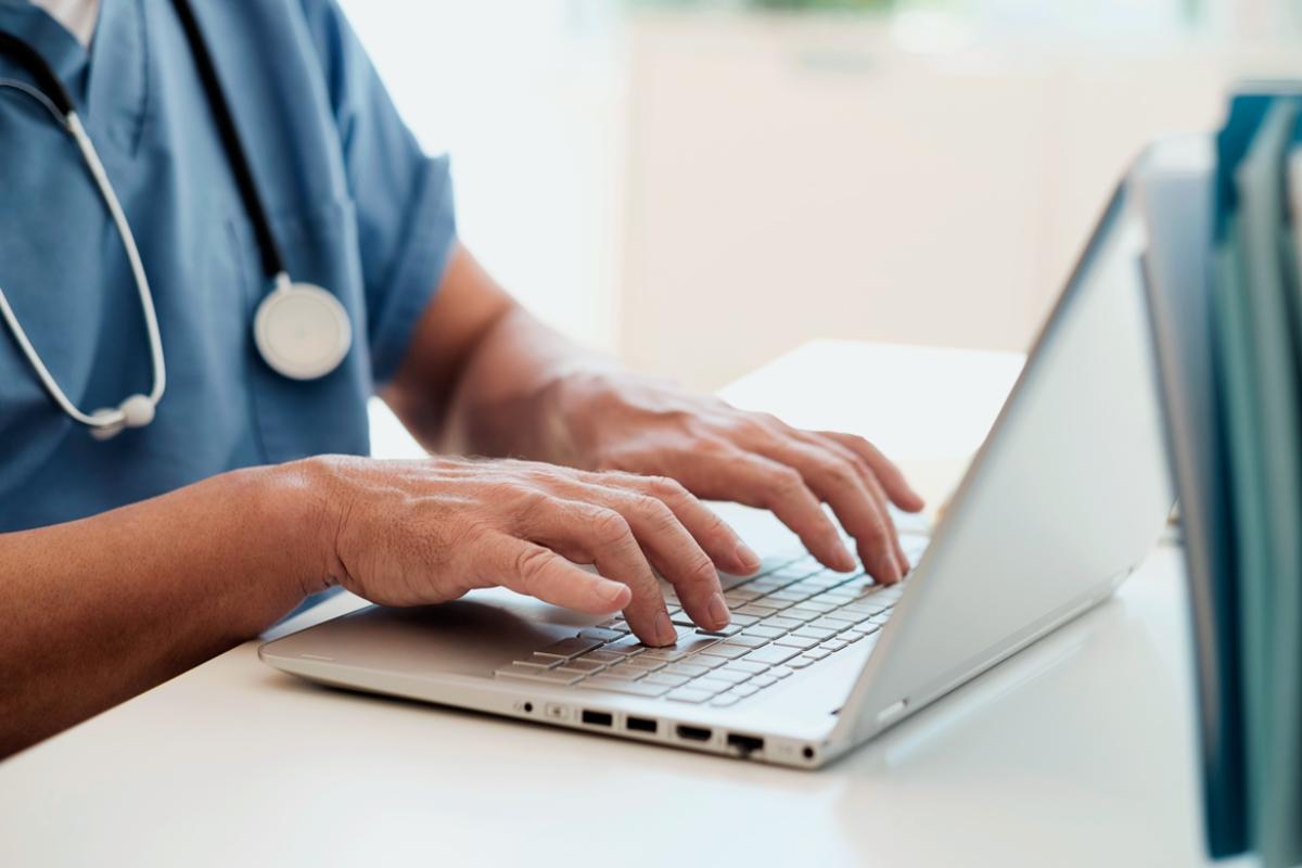 Closeup of medical professional with hands on laptop.
