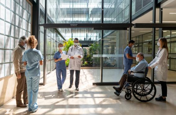 Hospital entrance with a number of doctors, nurses, patients, and other people entering and exiting.