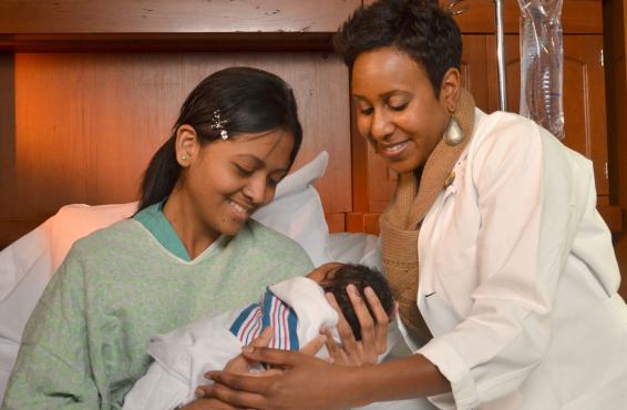 Veronica Gillispie-Bell, MD handing a new mother in a hospital bed her newborn.