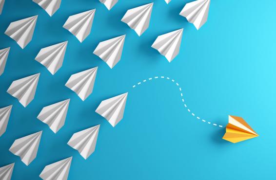 Pack of paper airplanes with one flying away in a different direction