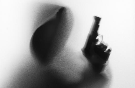 Image of a person's face in shadow holding a gun