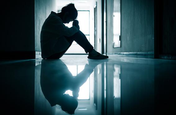 Young woman sitting on the floor in a hallway with her head on top of her knees.