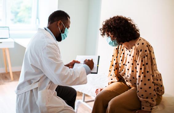 Physician going over examination notes with patient, both wearing masks. 